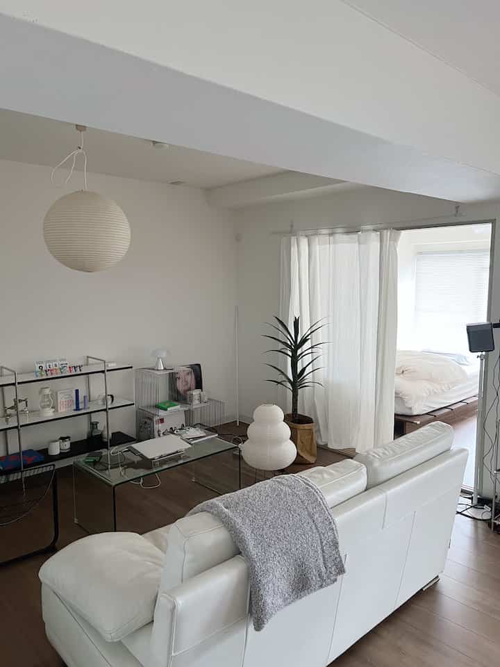 White and natural tone living room featuring large sofa, glass coffee table, and pendant light, creating a clean, natural atmosphere