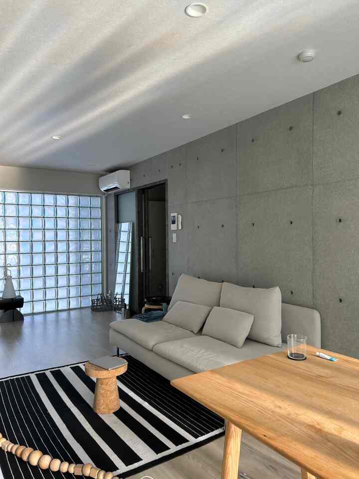 ナチュラルな色調のリビング、コンクリート壁とベージュのソファ、コルク製のサイドテーブルが配置された落ち着いた雰囲気の空間