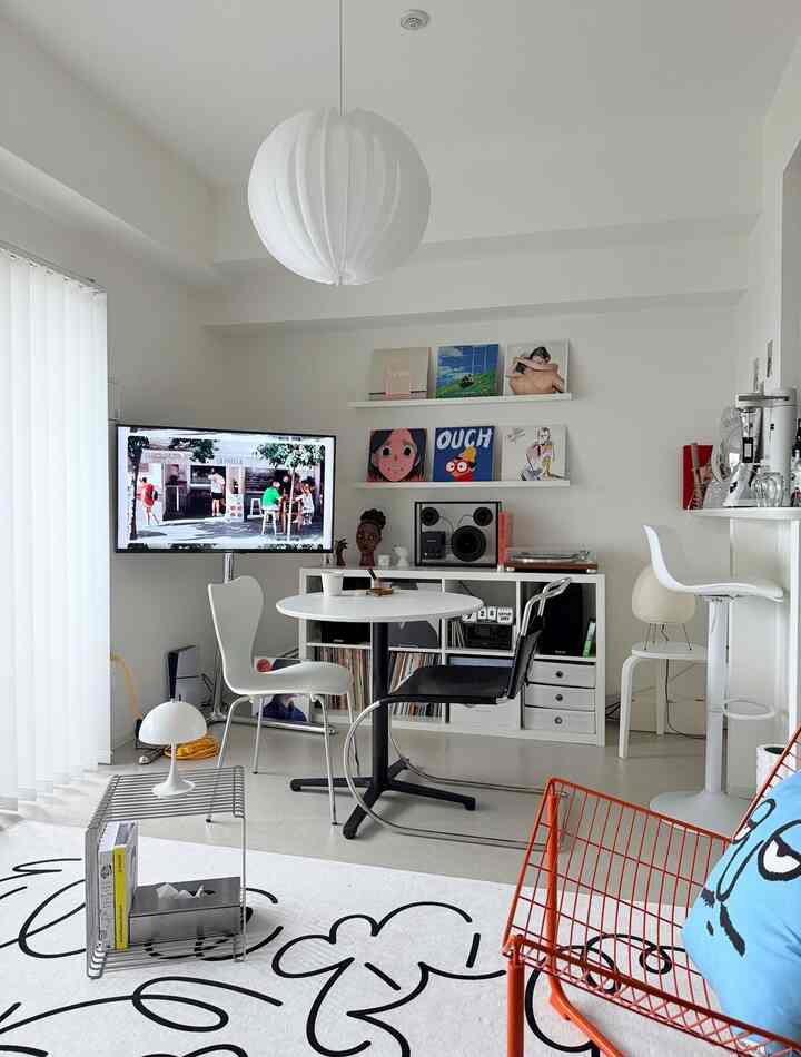White-toned living room featuring round dining table, mixed chairs, LP records, and coffee equipment creating a modern vibe