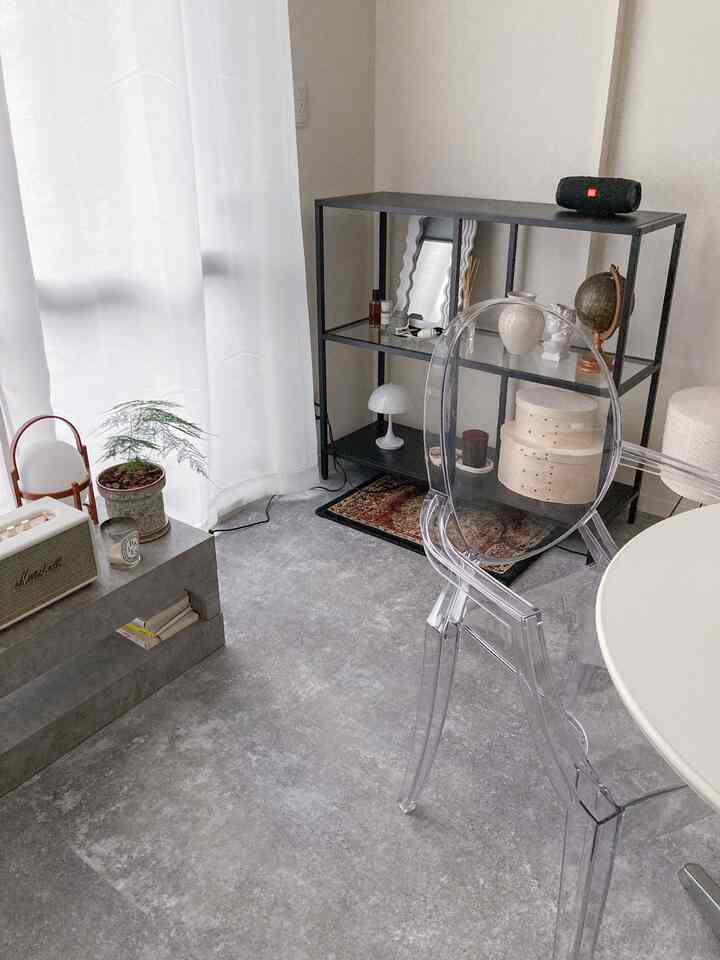 モノトーンの1LDKリビング、クリアチェアと黒い棚、白いカーテンが配置されたシンプルな印象的な空間