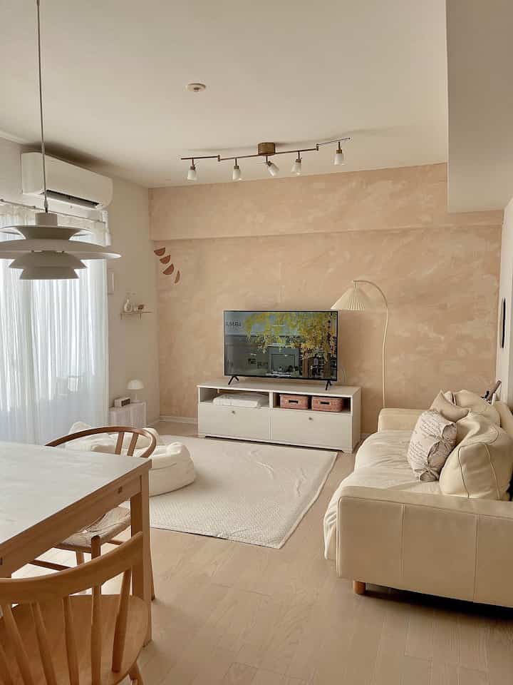 Warm beige toned natural style living room featuring a beige leather sofa, white curtains, and wooden dining table