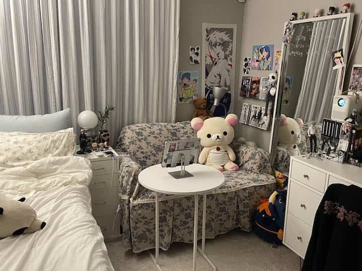柔らかなホワイトとブルーのトーンのコンパクトな寝室、花柄ソファと多彩なアニメポスターが印象的な居心地の良い一人暮らしの空間