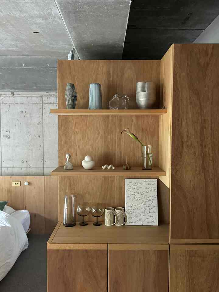 ナチュラルな色調のワンルームリビング、木製の棚に花瓶やカップが並ぶモダンなインテリア