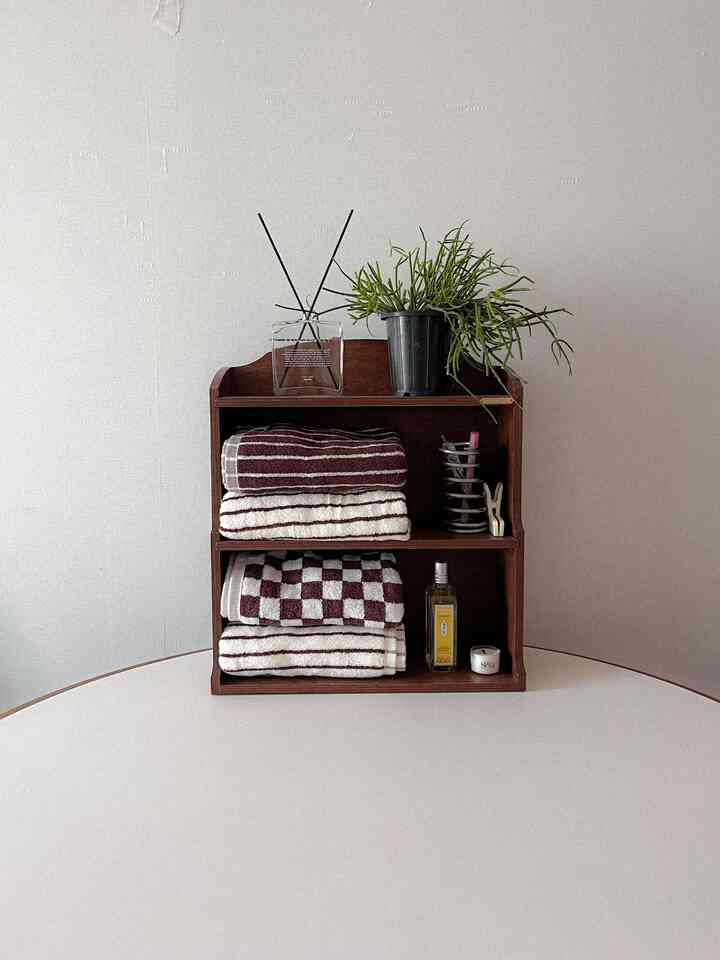 Clean white-toned table featuring a wood tone shelf with folded towels and a potted plant, creating a cozy atmosphere