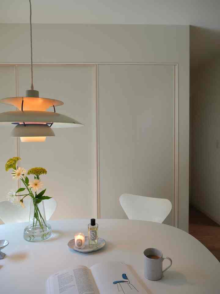 白とナチュラルカラーのダイニングルーム、ペンダントライト、花瓶、キャンドルが配置された印象的な空間