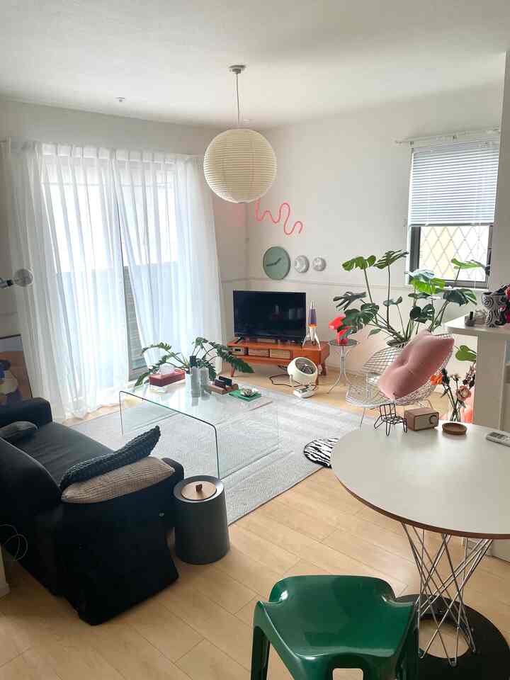 白と木目調のリビング、黒のソファと透明なコーヒーテーブル、緑の植物が配置された雰囲気のあるミッドセンチュリーモダン空間