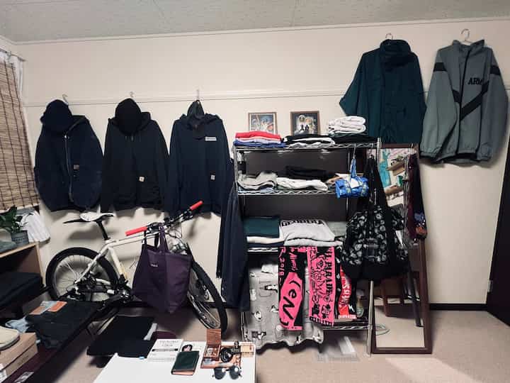 Natural tones and black colors blend in a compact single household room featuring clothes hangers, a bicycle, and metal shelving organized efficiently