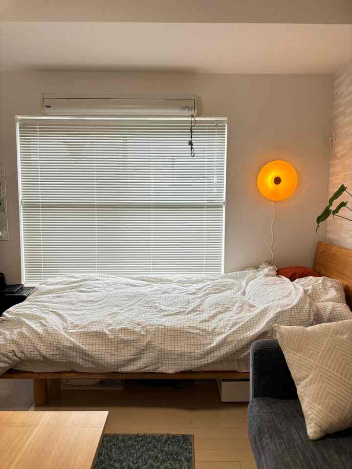 White and wood tone 1K bedroom featuring a comfortable bed, blinds, and warm wall lamp creating a cozy atmosphere