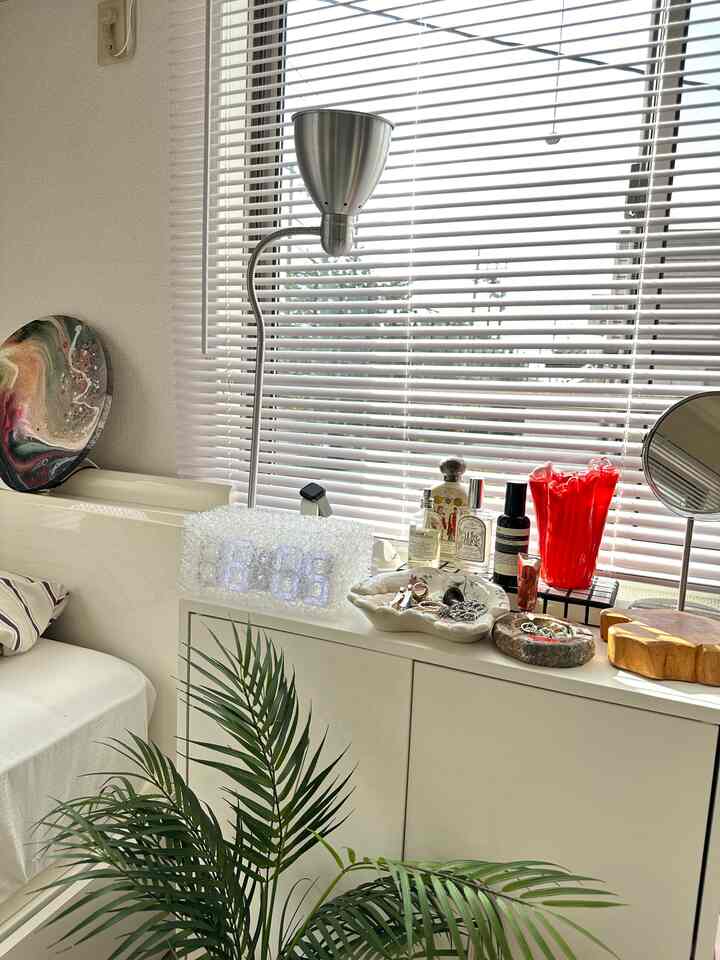White-toned living room with white sofa, a Leirstad floor lamp, digital clock on cabinet, and a plant creating cozy atmosphere