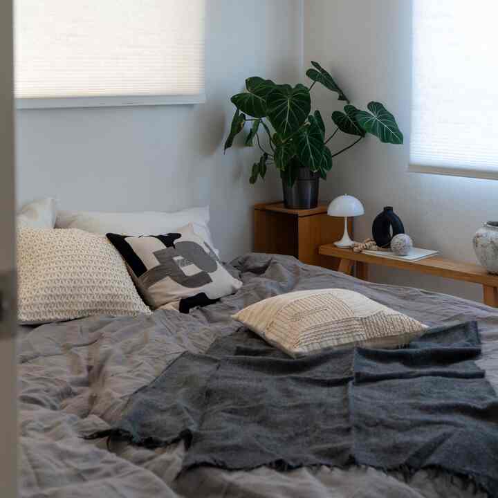 A cozy monotone bedroom with natural wood tones, featuring a comfortable bed with assorted pillows and a green plant
