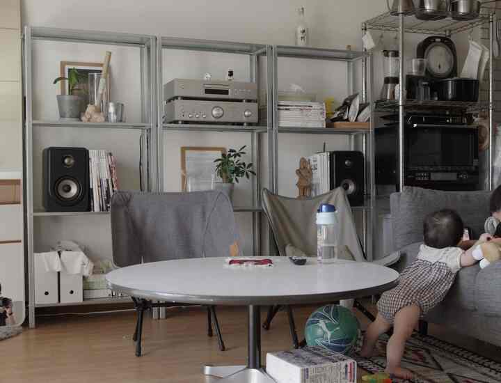 グレーと白のトーンのリビング、ラウンドテーブルとアウトドアチェアが配置され、ソファ周りで遊ぶ子供たちがいる自然な雰囲気のインテリア