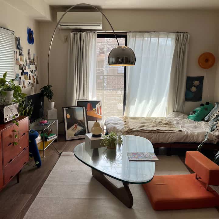 ナチュラルな木目調と白いカーテンが調和する8畳のワンルーム、ミッドセンチュリーモダン家具と植物が配置された雰囲気のあるインテリア