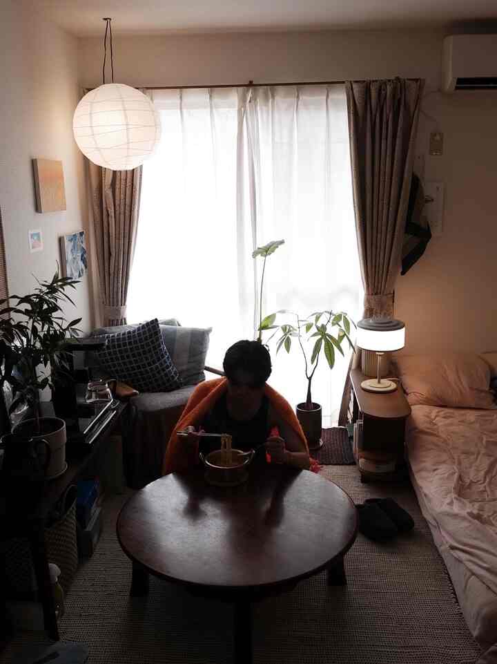 Beige and natural toned small living room featuring a round wooden table, bed, and plants creating a cozy atmosphere
