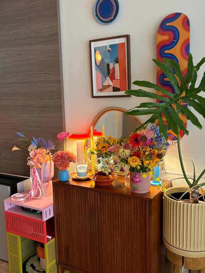 Colorful vases and plants arranged on a wooden display cabinet with a wall mirror in a cozy dining space