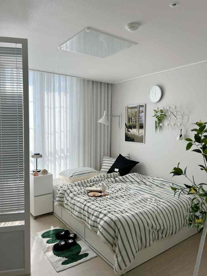 ホワイトを基調としグリーンのアクセントがある寝室、ストライプの寝具とヘッドレスベッド、グリーンのラグが配置された雰囲気のある空間