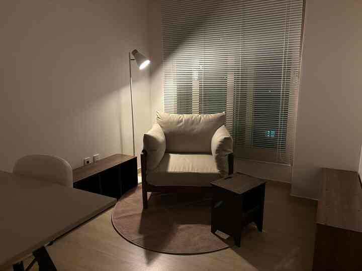 Beige and wood tones harmonize in a cozy single-person living room featuring a floor lamp and blinds.