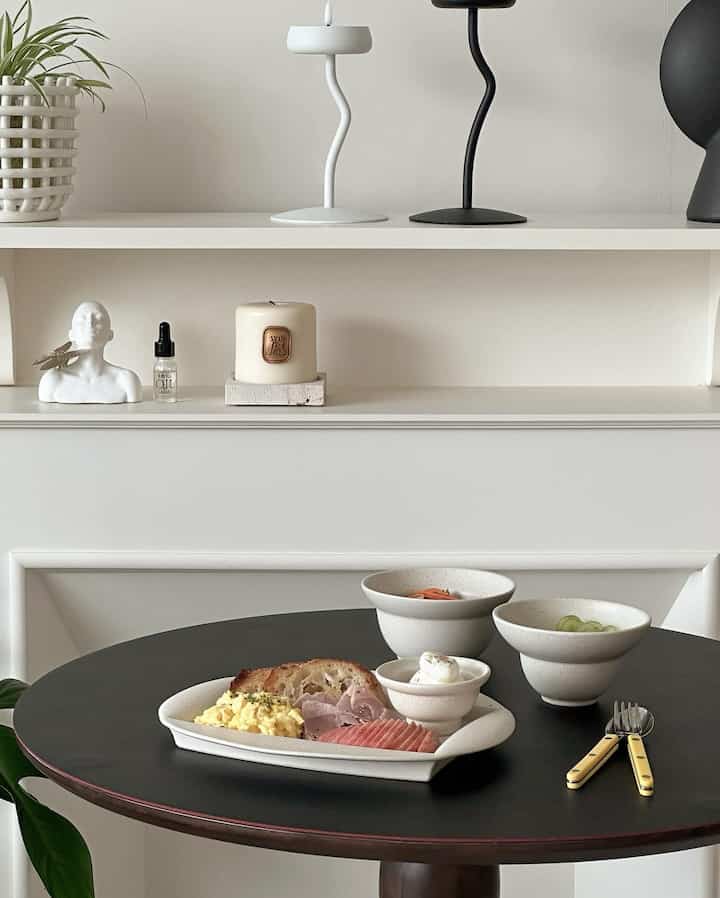 Minimal cafe-style dining room with harmonious white and black tones, featuring a round dining table set with bowls and plates neatly arranged