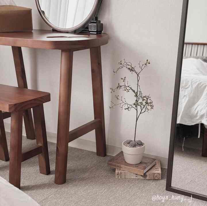 ベージュと木目調の狭い部屋、木製の一人用ダイニングテーブルセットと鏡、植物が配置された雰囲気あるインテリア