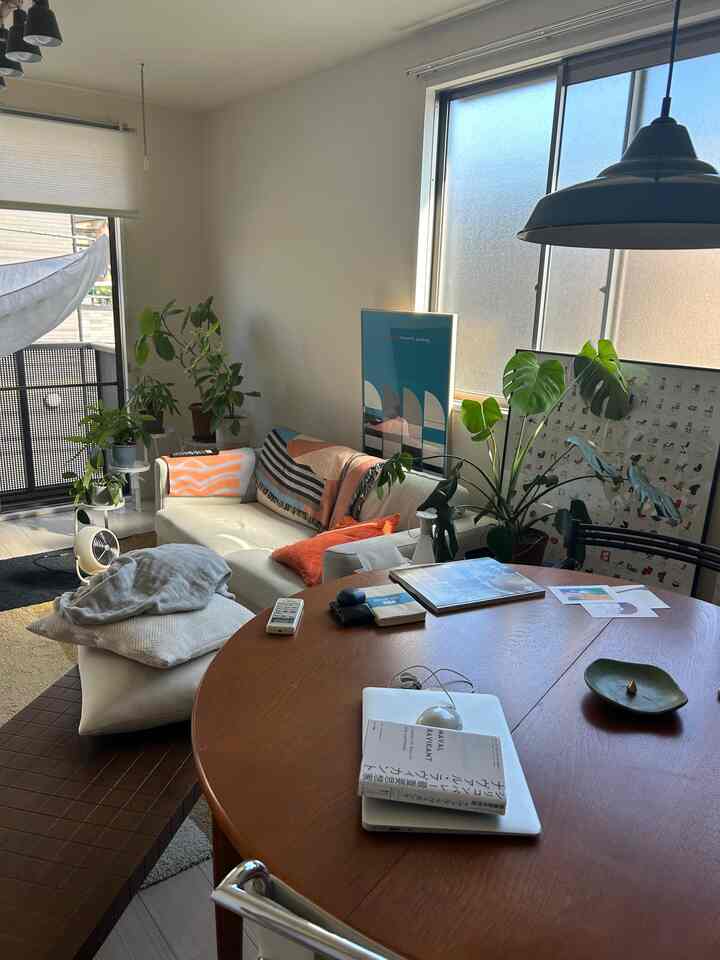 白い壁とブラウンの丸いダイニングテーブルがあるリビング、ベージュのソファと多数の植物が配置された雰囲気のあるミッドセンチュリーモダンの空間