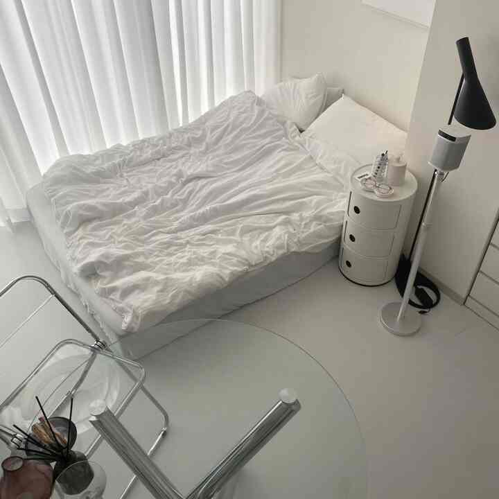ホワイトと透明素材の調和が取れたワンルーム寝室、ミッドセンチュリーモダン家具と整然としたナイトテーブル、フロアランプが配置された落ち着いた空間