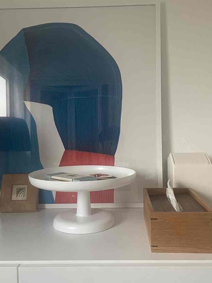 白と木目調の玄関、抽象的なポスターとトレイが印象的に配置されたミニマルなインテリア