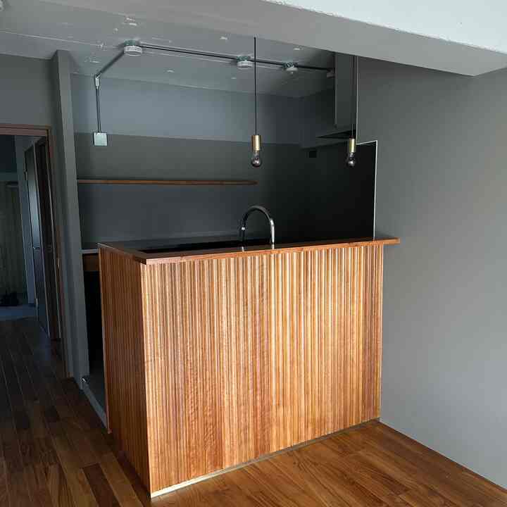 グレー壁と木目調のクラシックリブパネルのキッチン、ペンダントライトが吊るされたミッドセンチュリーモダンの雰囲気のあるインテリア