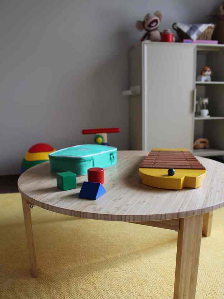 Yellow rug and wooden round table in a kids' room interior featuring toys and storage cabinet
