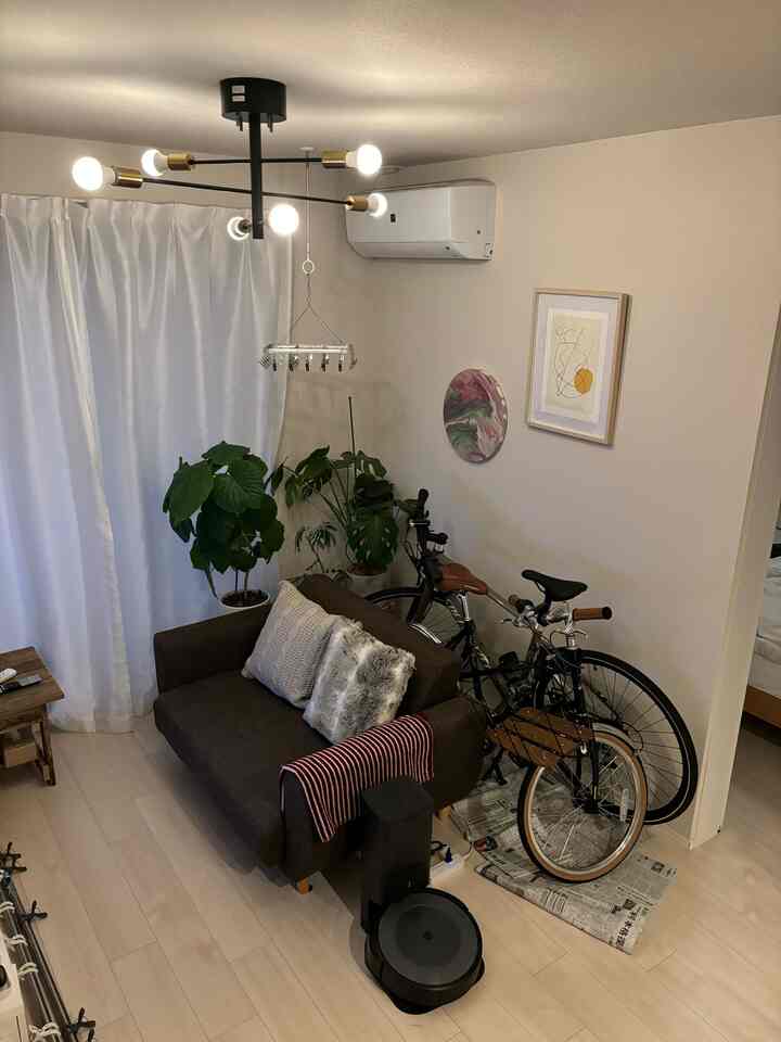 ベージュ色の壁と明るい木目調床のコンパクトなリビング、ブラウンの2人掛けソファと観葉植物、自転車2台が置かれたナチュラルなインテリア