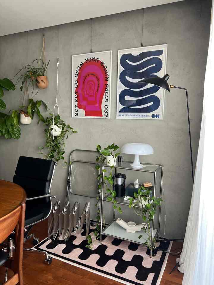 Gray concrete wall living room featuring metal rack, black office chair, and mid-century modern posters with a cozy, natural atmosphere