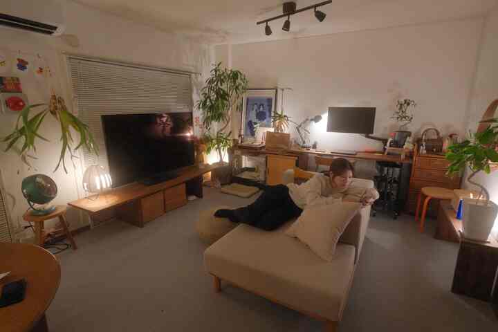 ナチュラルな色調のリビング、ベージュのソファと多数の植物、間接照明が配置された雰囲気のある空間