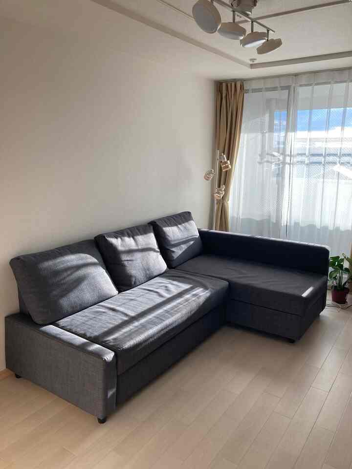 明るくナチュラルな雰囲気のリビング、ダークグレーのソファベッドが大きな窓際に配置されている