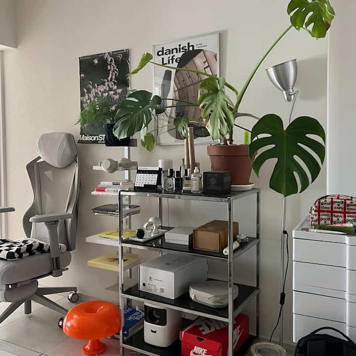 ナチュラルカラーとグレー調のリビング、モダンヴィンテージスタイルのメタルシェルフとゲーミングチェア、モンステラが配置された印象的な空間