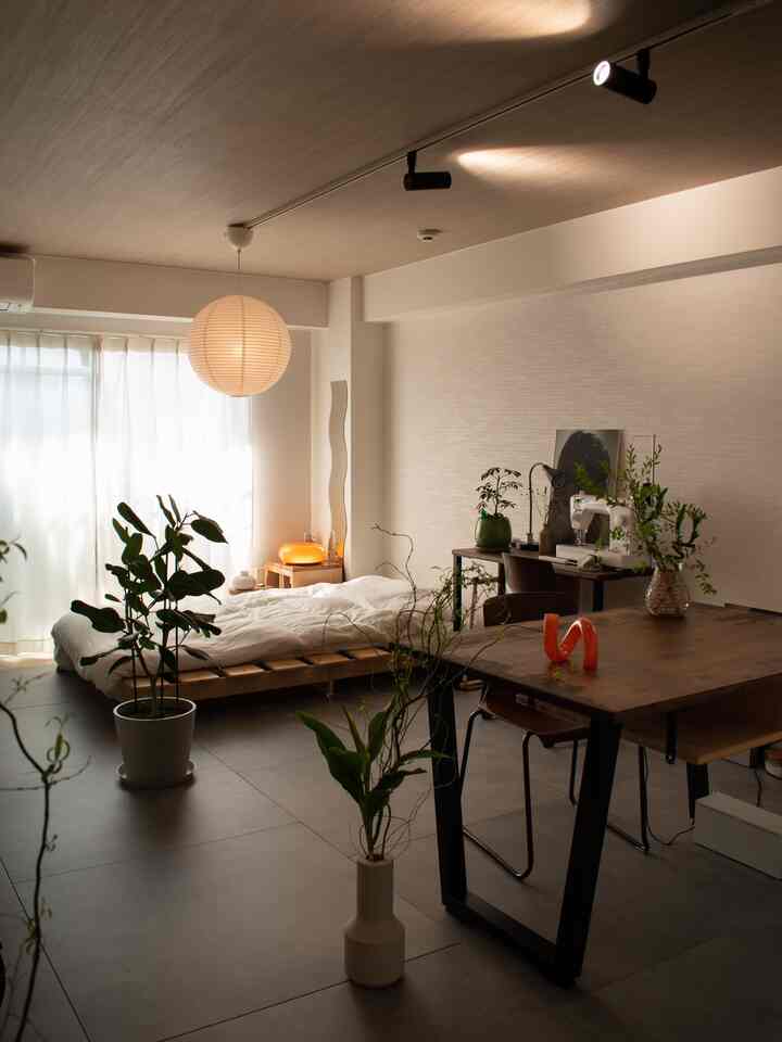 ナチュラルカラーのワンルーム、木製家具と多様な植物、ペンダントライトが配置された雰囲気のある空間