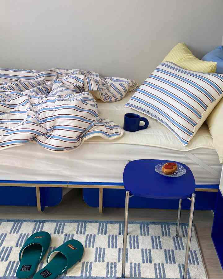 White and blue toned kids' room featuring striped bedding and blue stool creating a cozy atmosphere