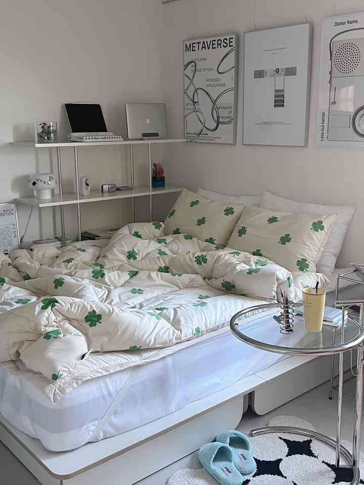 白を基調とした寝室で、緑のクローバー柄の寝具とミッドセンチュリーモダンのポスターが配置されたモダンでコンパクトな雰囲気のあるインテリア