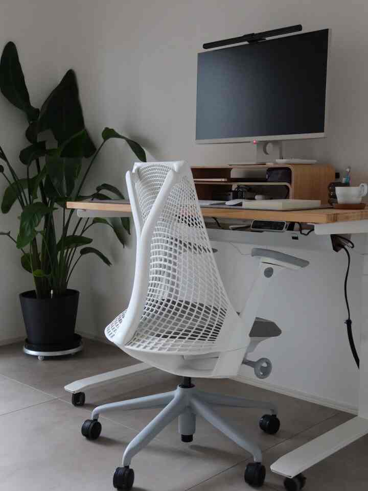 白とナチュラルカラーのワークスペース、セイルチェアと電動昇降デスクが配置された清潔感のある現代的なインテリア