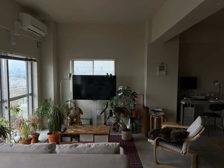 A modern natural living room with white walls, natural brown furniture, sofa, and abundant plants creating a cozy atmosphere