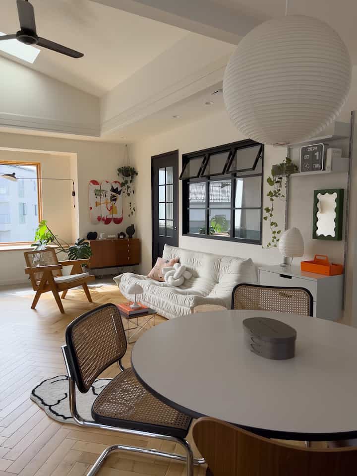 白色のトーンと木目調の床のリビング、大きな丸いペンダントライトとソファ、木製のアームチェアが配置された自然な雰囲気のあるインテリア