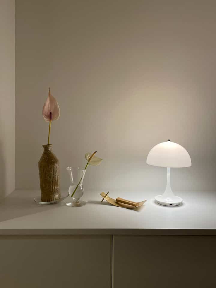 ホワイトトーンの玄関、パンテラのテーブルランプとシンプルな花瓶が配置された清潔感のある空間