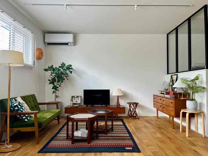 木目調とグリーンが映えるミッドセンチュリーモダンのリビング、ヴィンテージ家具とラグが調和する印象的な空間