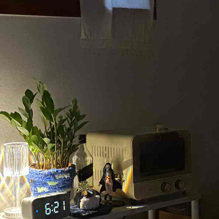 ベージュのレトロなトースターと青いニットカバーの植物、ムードライトとデジタル時計が置かれた居心地の良いキッチンの棚の空間