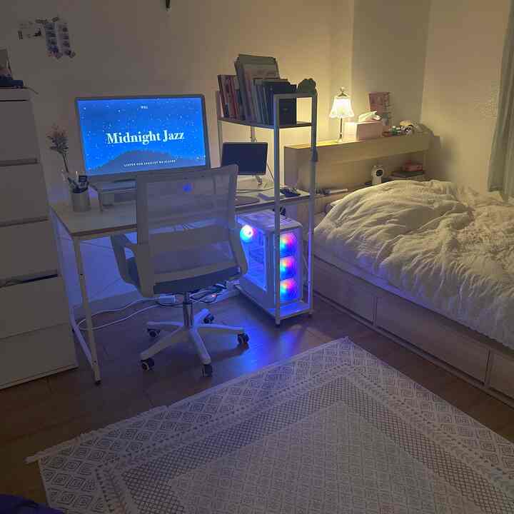 ホワイトとウッドトーンを基調とした寝室のホームオフィス空間、ベッドとコンピューターデスク、オフィスチェアが配置された居心地の良い個人空間