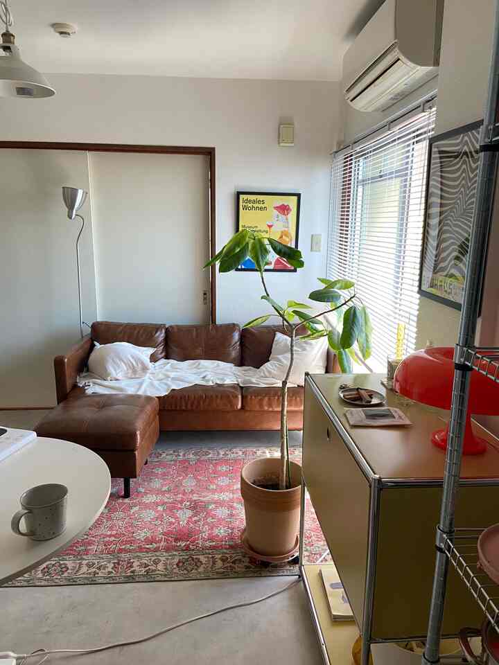 ブラウンレザーのソファと赤い柄のラグ、大きな観葉植物と照明が配置されたミッドセンチュリーモダンのリビングルーム