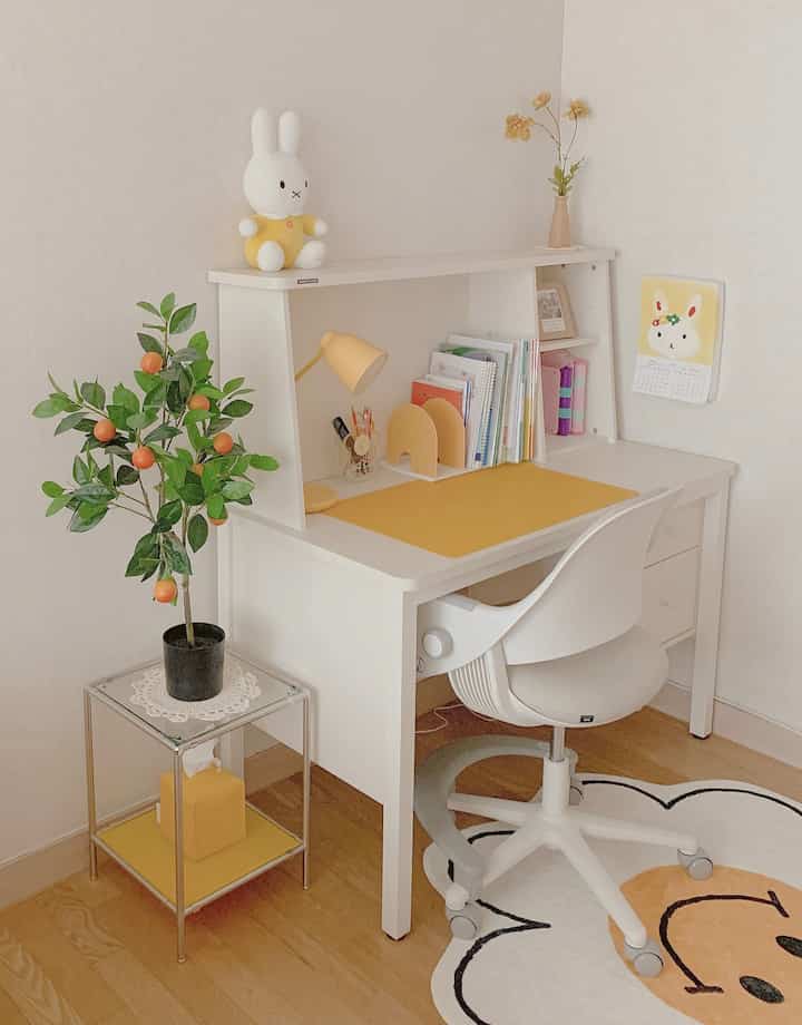 明るい黄色のアクセントが特徴の子供部屋の学習机スペース、白い家具とかわいらしい小物が配置されたシンプルで清潔感のあるインテリア