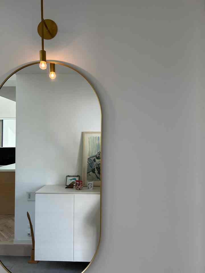 白と茶色の色調の玄関、壁付けライトと大きな縦長の鏡が配された印象的な空間