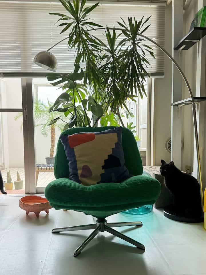 明るい白い床と緑のアームチェア、フロアランプ、ペットの猫と植物があるモダンなリビングスペース