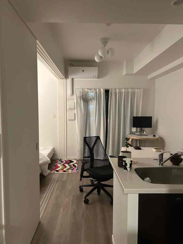 白と茶色のトーンのワンルーム、デスクとオフィスチェアが配置された清潔感のあるコンパクトな空間