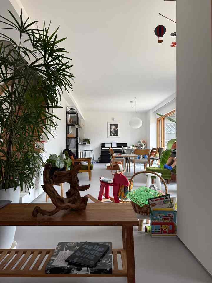 ナチュラルカラーとホワイトの玄関からリビングへの空間、子供の玩具と観葉植物が配置された温かみのある開放的なインテリア