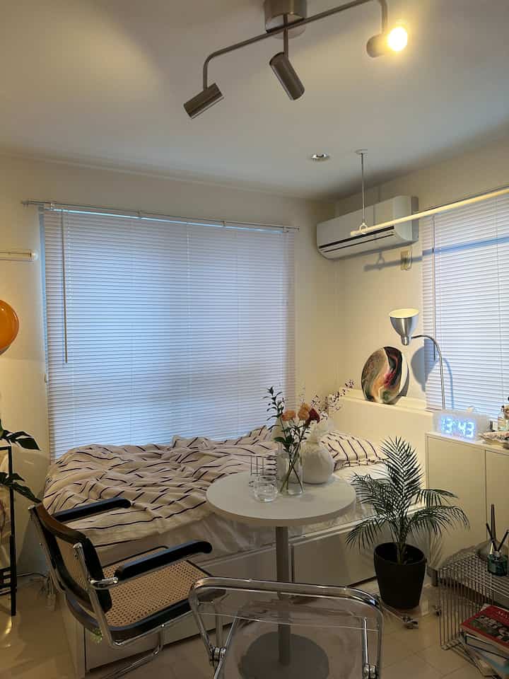 白と茶色を基調とした寝室、ラタンチェアと植物が配置されたナチュラルモダンな雰囲気のインテリア