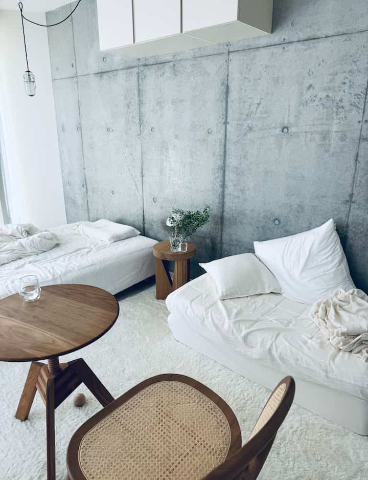 White and brown tone bedroom-living area featuring concrete wall and natural wood furniture, creating a simple and natural modern atmosphere